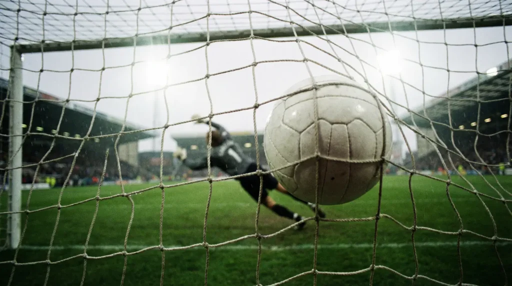 Bola de futebol entrando na rede do gol vista de dentro da baliza